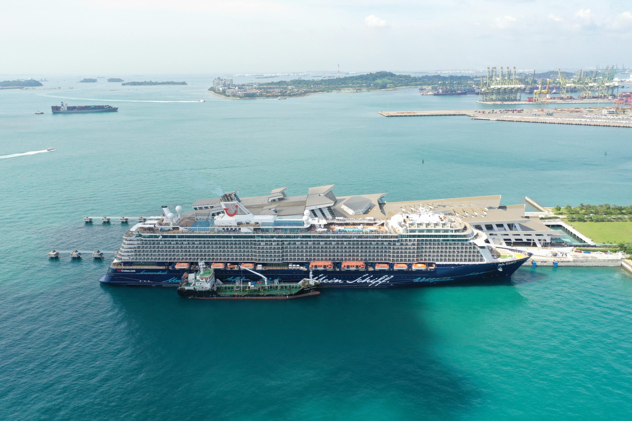 Home Cruise ship Mein Schiff 5 moored at a vibrant Singapore harbor under clear skies.
